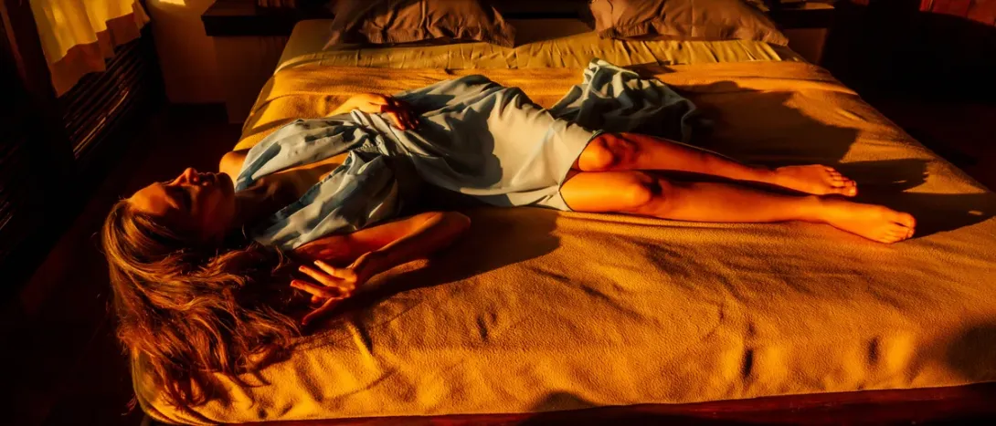 A woman lying across a bed in warm light