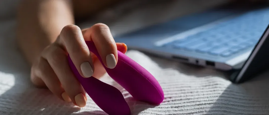 A hand holding a small pink toy next to a laptop