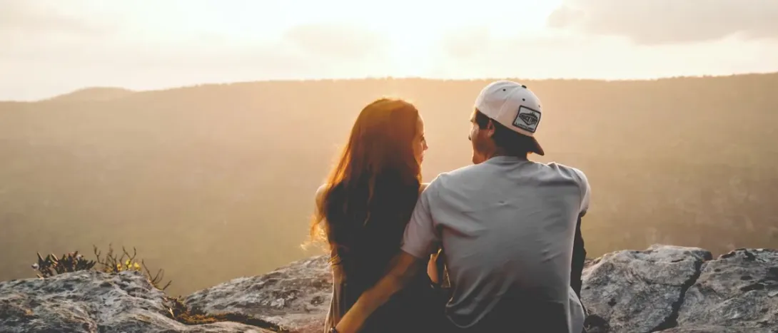 A couple sitting on a rock at sunset