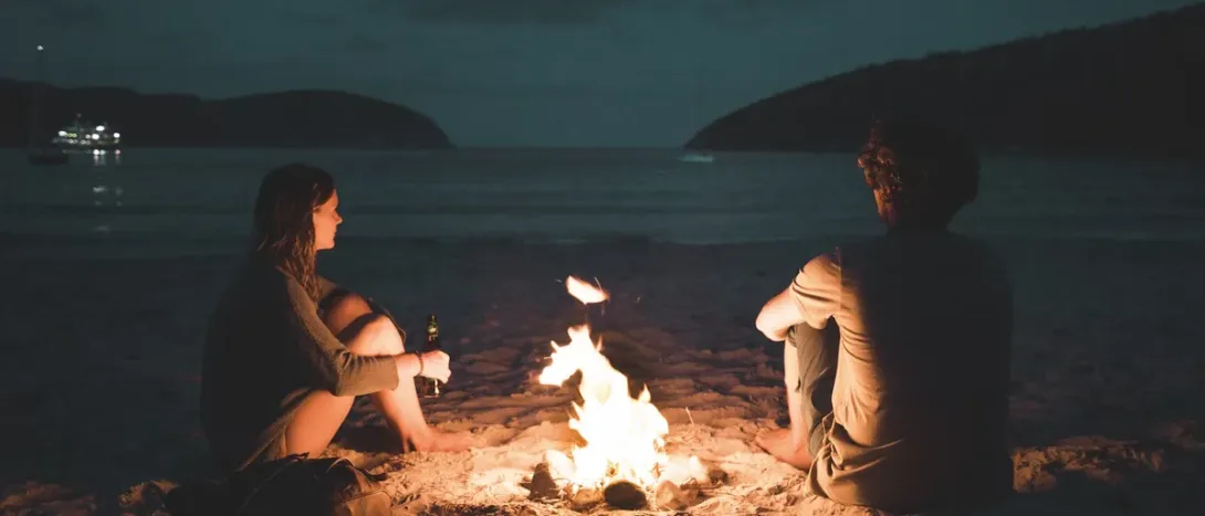 Two people by a campfire on the shore at dusk
