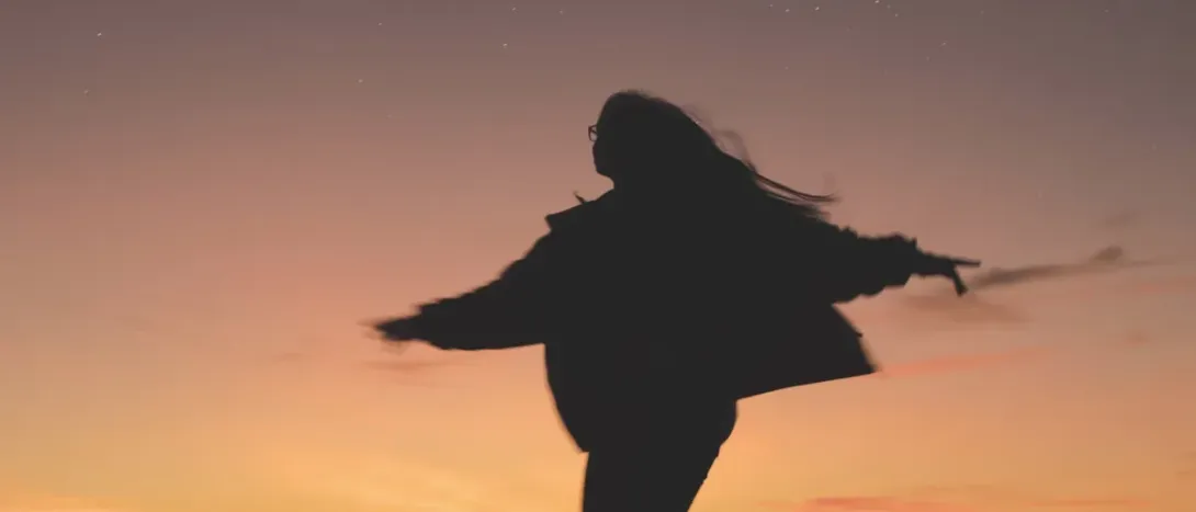 A woman's silhouette with arms open at sunset