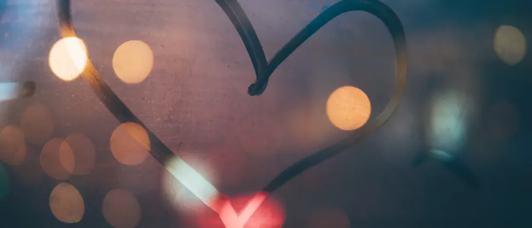A heart drawn on a window with city lights behind it