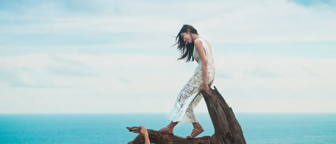 A woman standing on driftwood by the sea