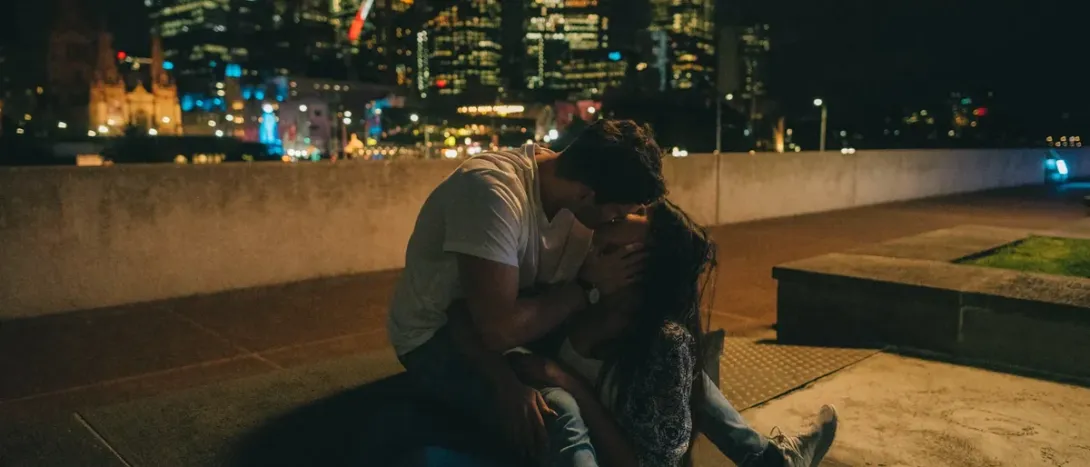 A couple kissing by the city at night