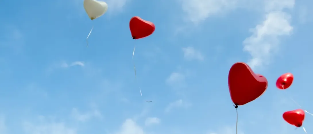 Red heart balloons against a blue sky