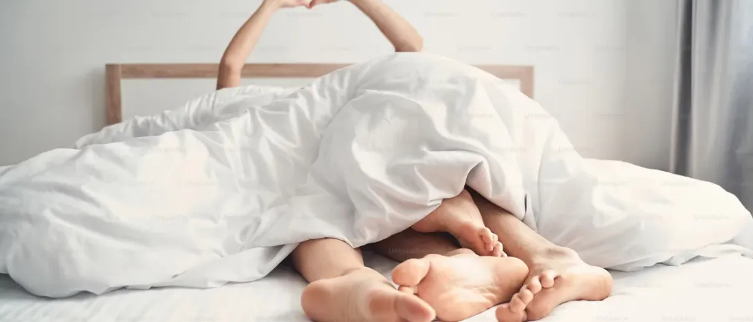 Two pairs of feet peeking out from under a duvet